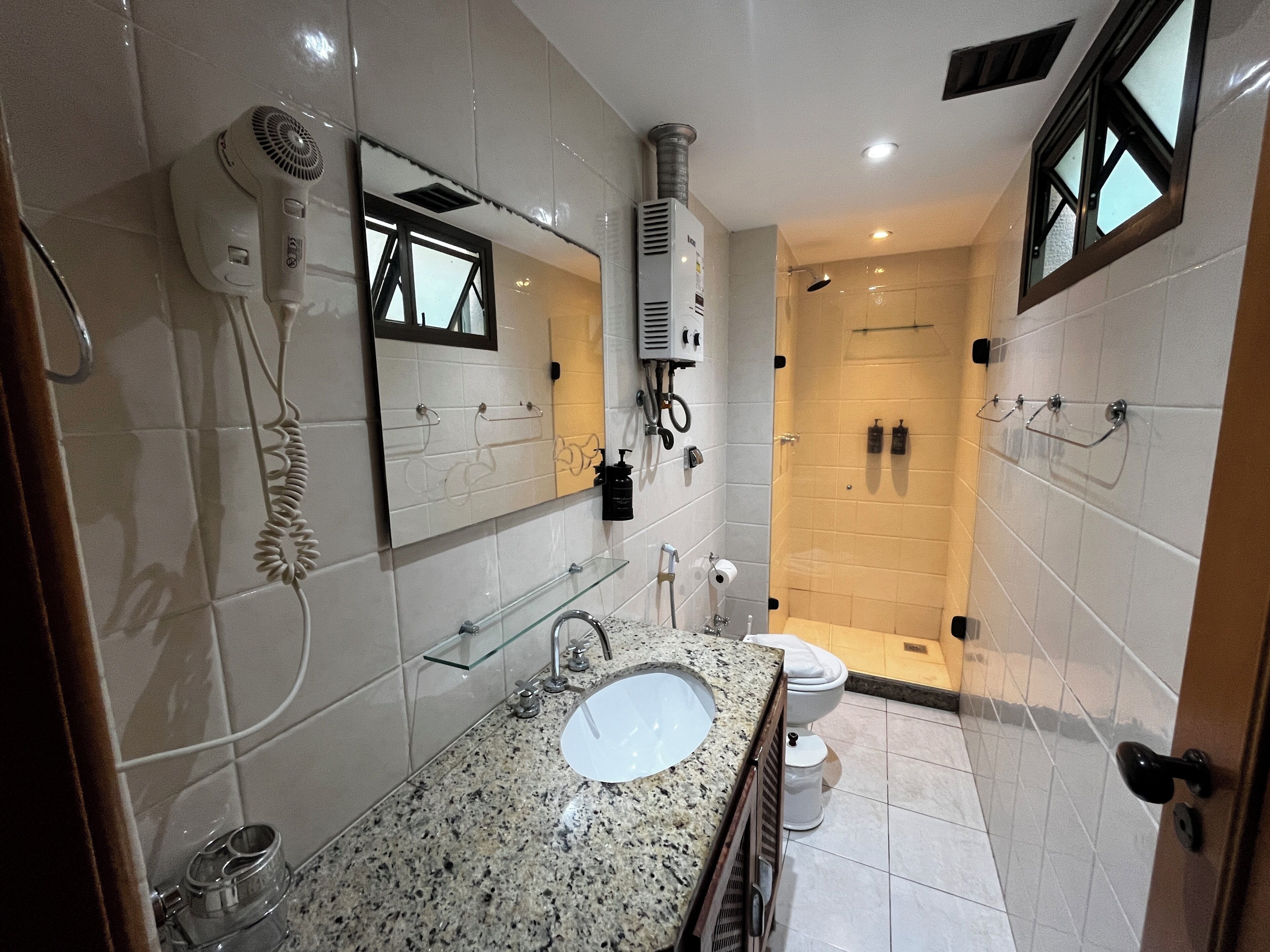 Un bagno dotato di lavandino, specchio, asciugacapelli, portasci, zona doccia e water.