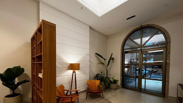 A modern lobby with a wooden bookshelf, two armchairs, a floor lamp, and a large arched glass door leading outside. - Mc Flats Ipanema Beach Star (Rio de Janeiro)