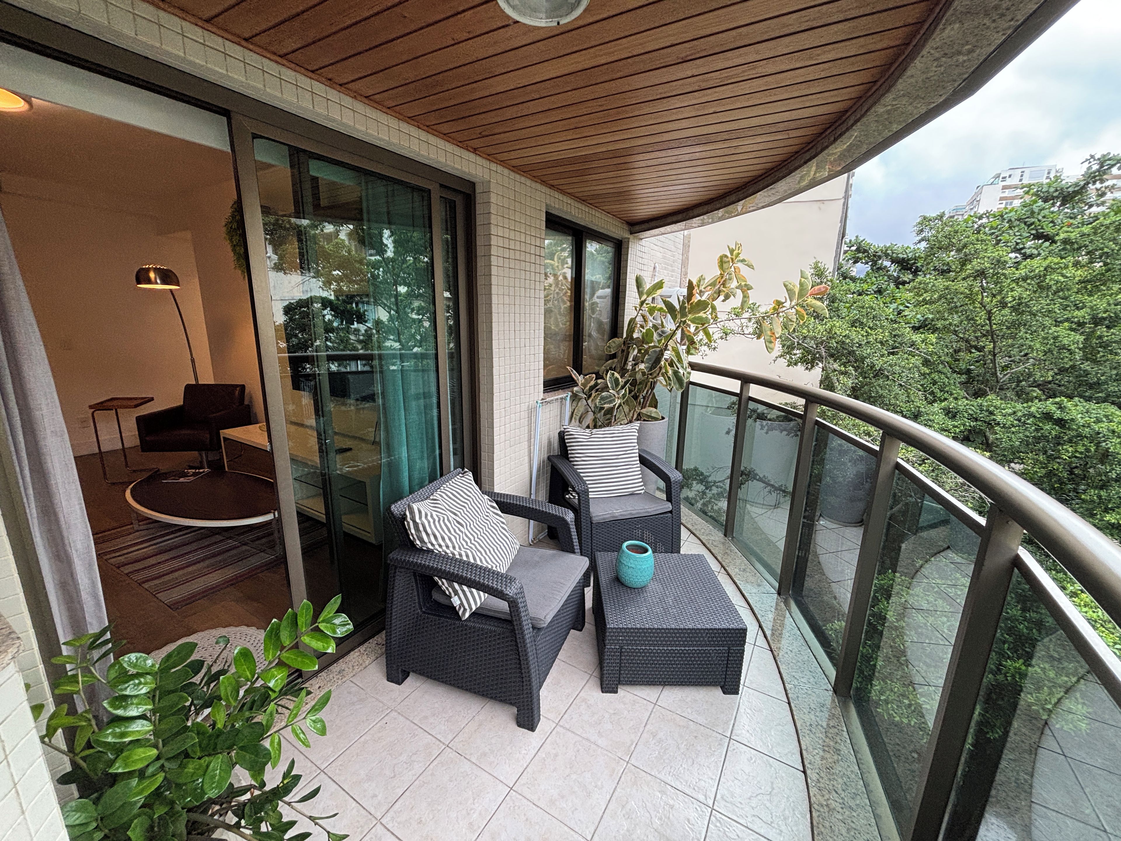 A balcony with wicker furniture, a potted plant, and a view of the cityscape.