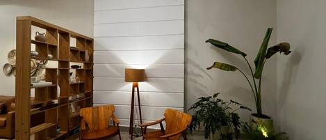 A room with a wooden bookshelf, two wooden chairs, a floor lamp, and a large potted plant.