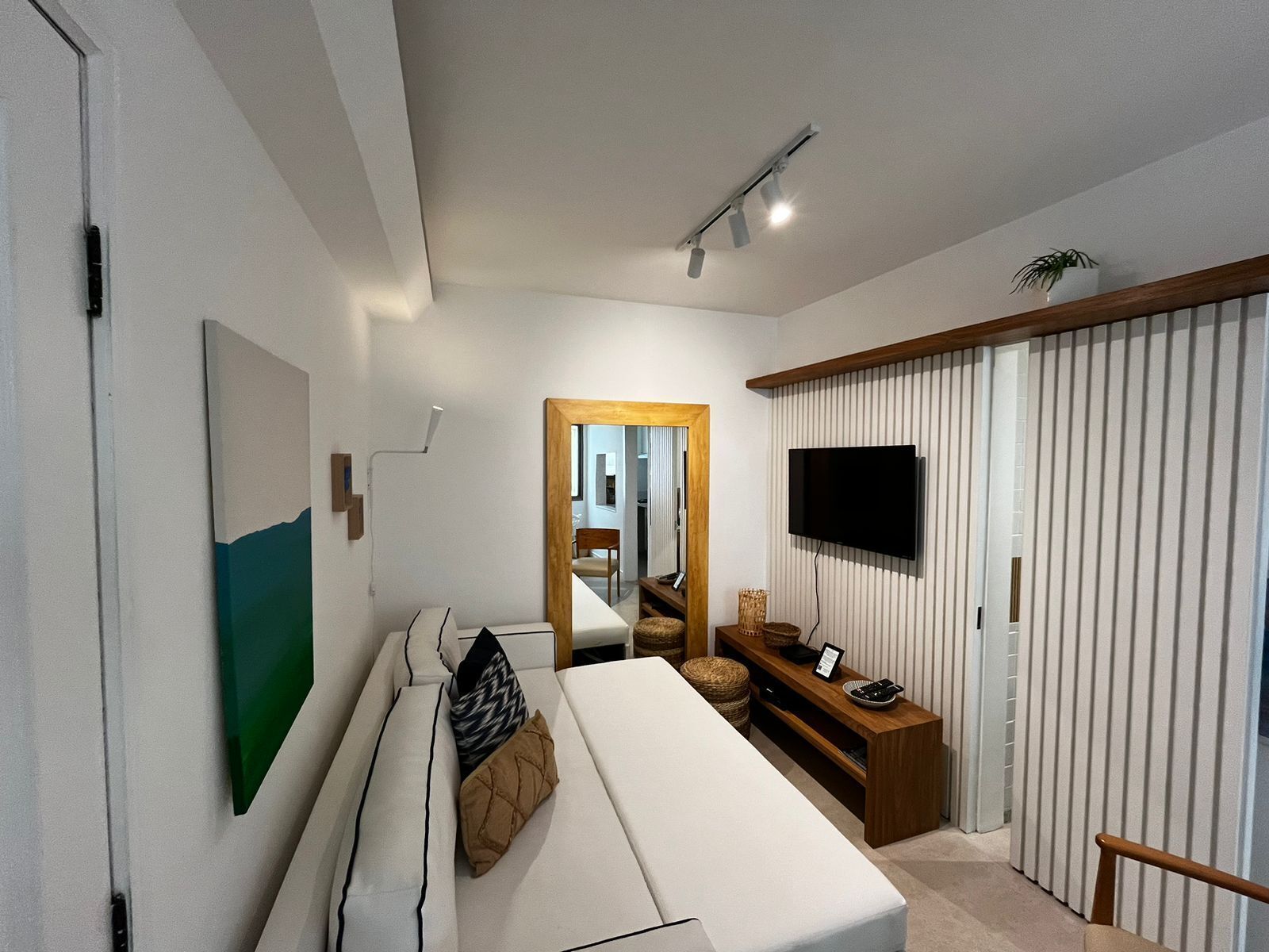 A modern bedroom with a bed, a television mounted on the wall, a mirror, and a wooden bench.