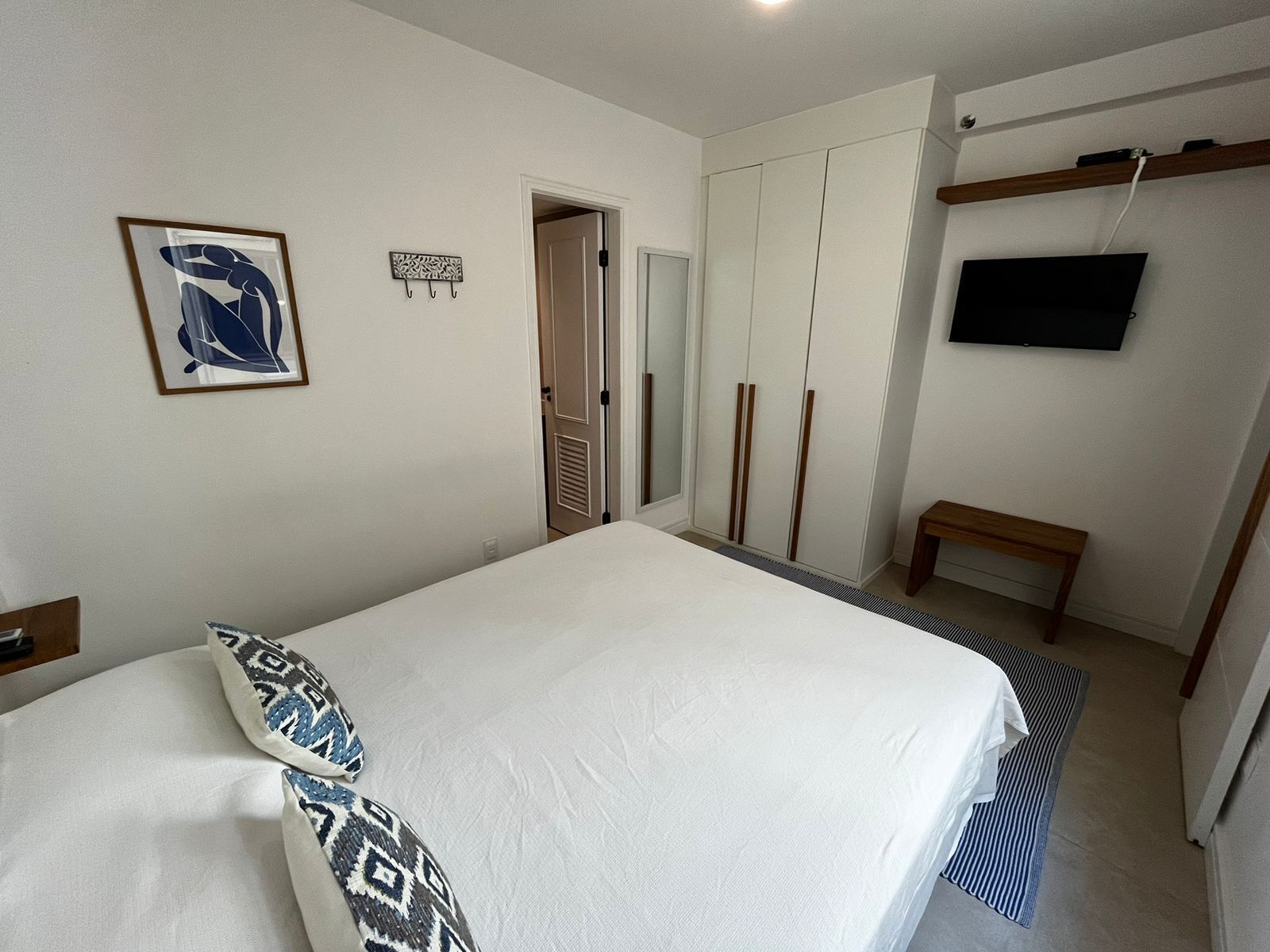 A bedroom with a bed, a wardrobe, a television, and a small bench.