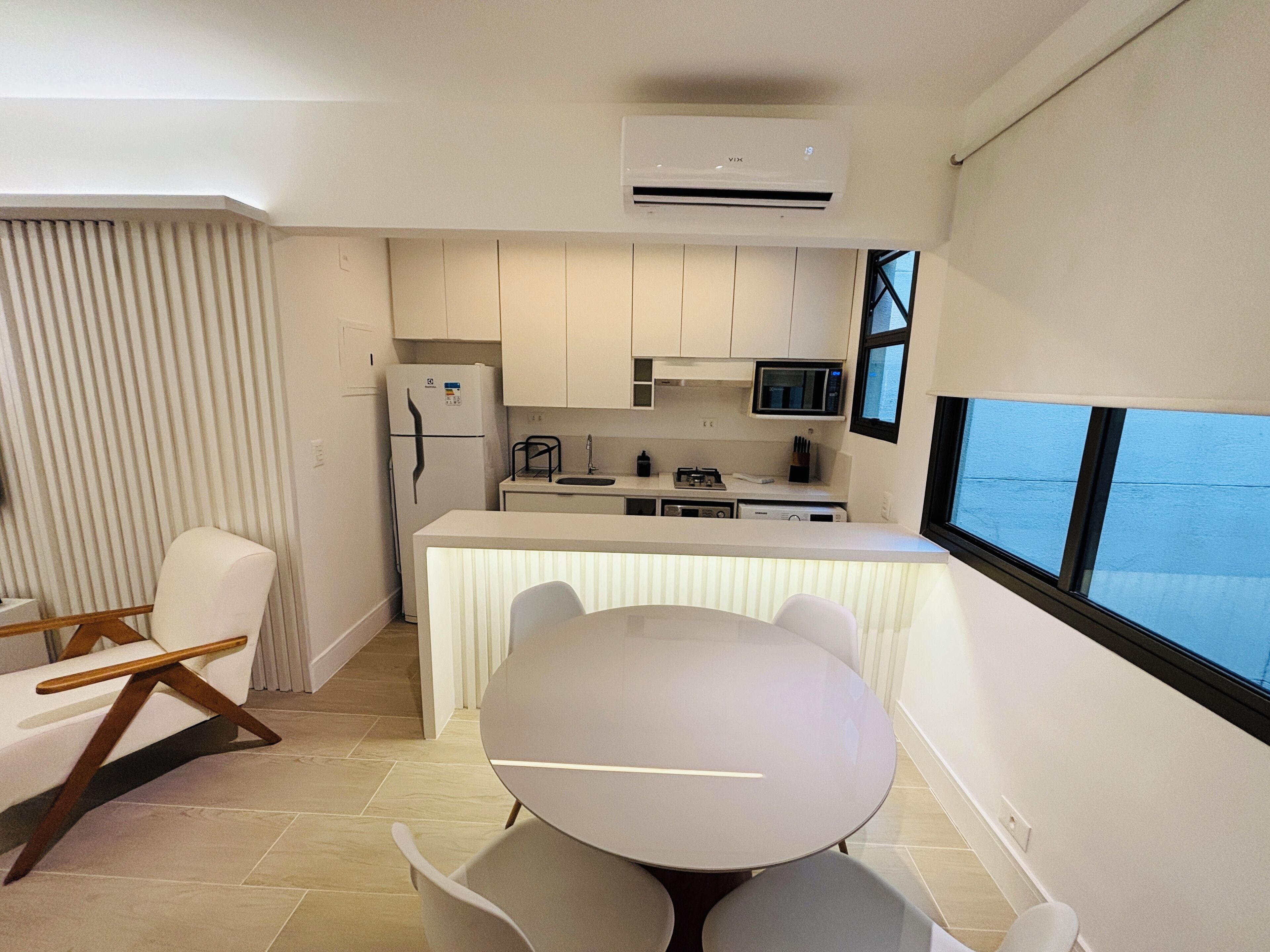 Una cocina moderna con armarios blancos, un refrigerador, un microondas y un comedor con una mesa redonda y sillas.