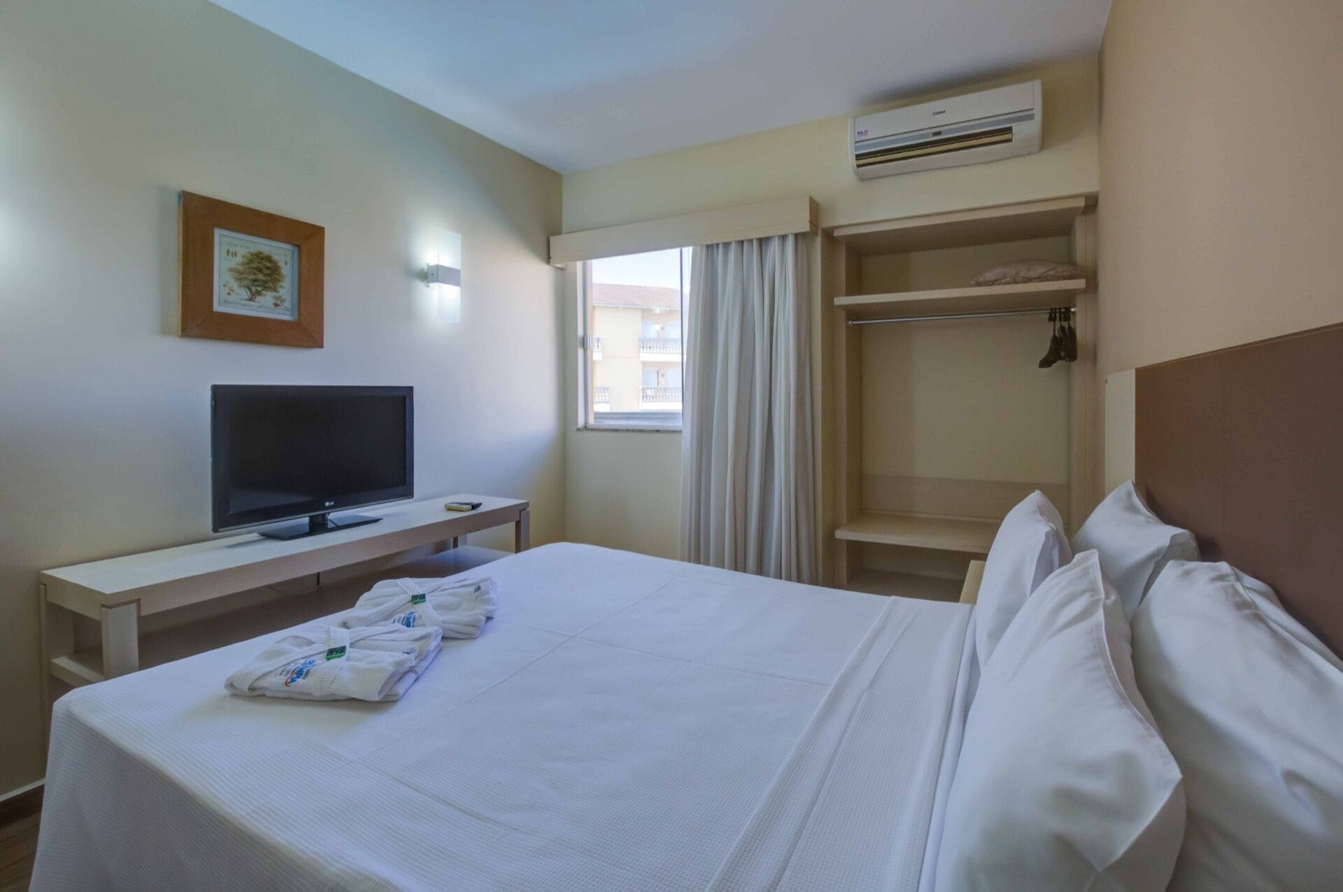 A hotel room with a bed, a TV, a wardrobe, and an air conditioning unit.