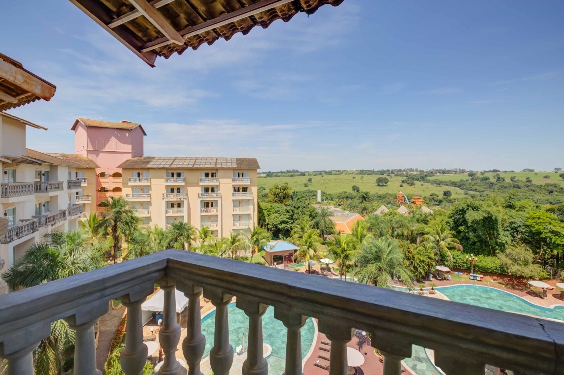 Un hotel de varios pisos, piscina y abundante vegetación al fondo.