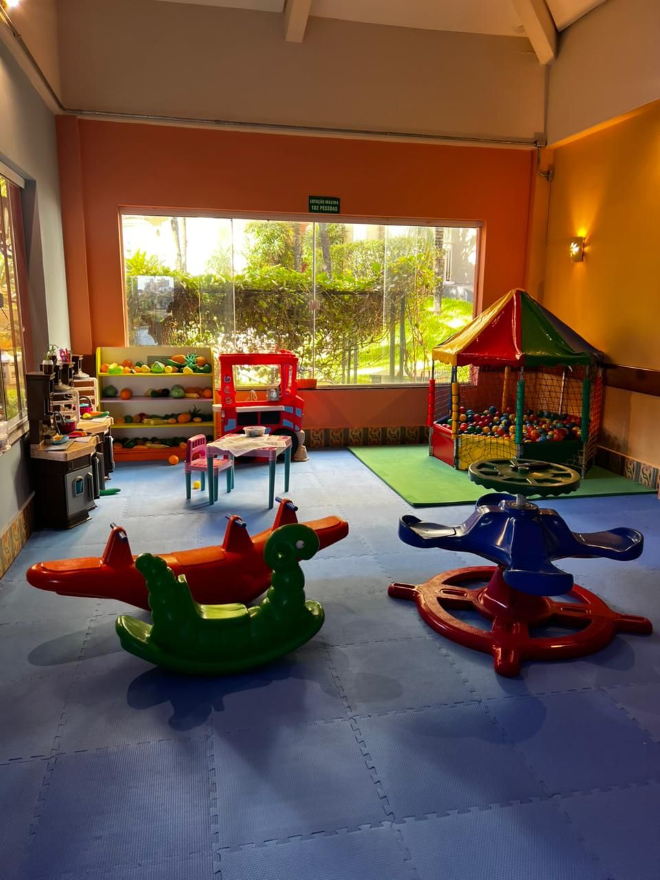 Un área de juegos para niños con un ventanal grande, mesas de juegos y equipo lúdico colorido.