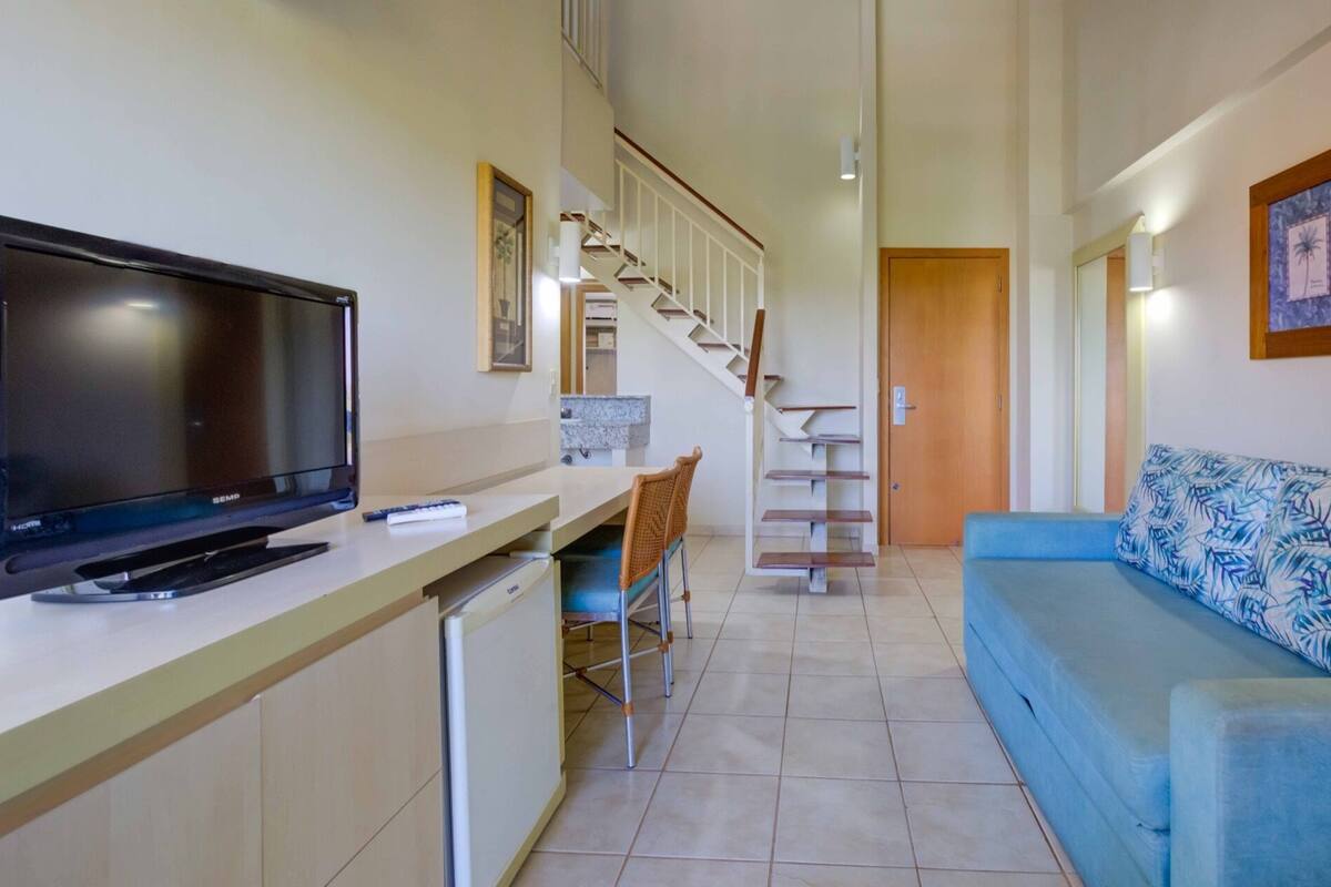 A compact living space with a kitchenette, a TV, a sofa, and a staircase leading to an upper level.