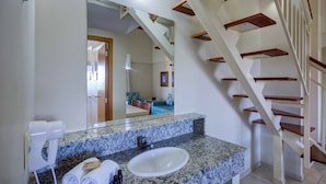 A bathroom with a granite countertop, a sink, a mirror, and a hairdryer. There is a staircase with wooden steps and a white railing.
