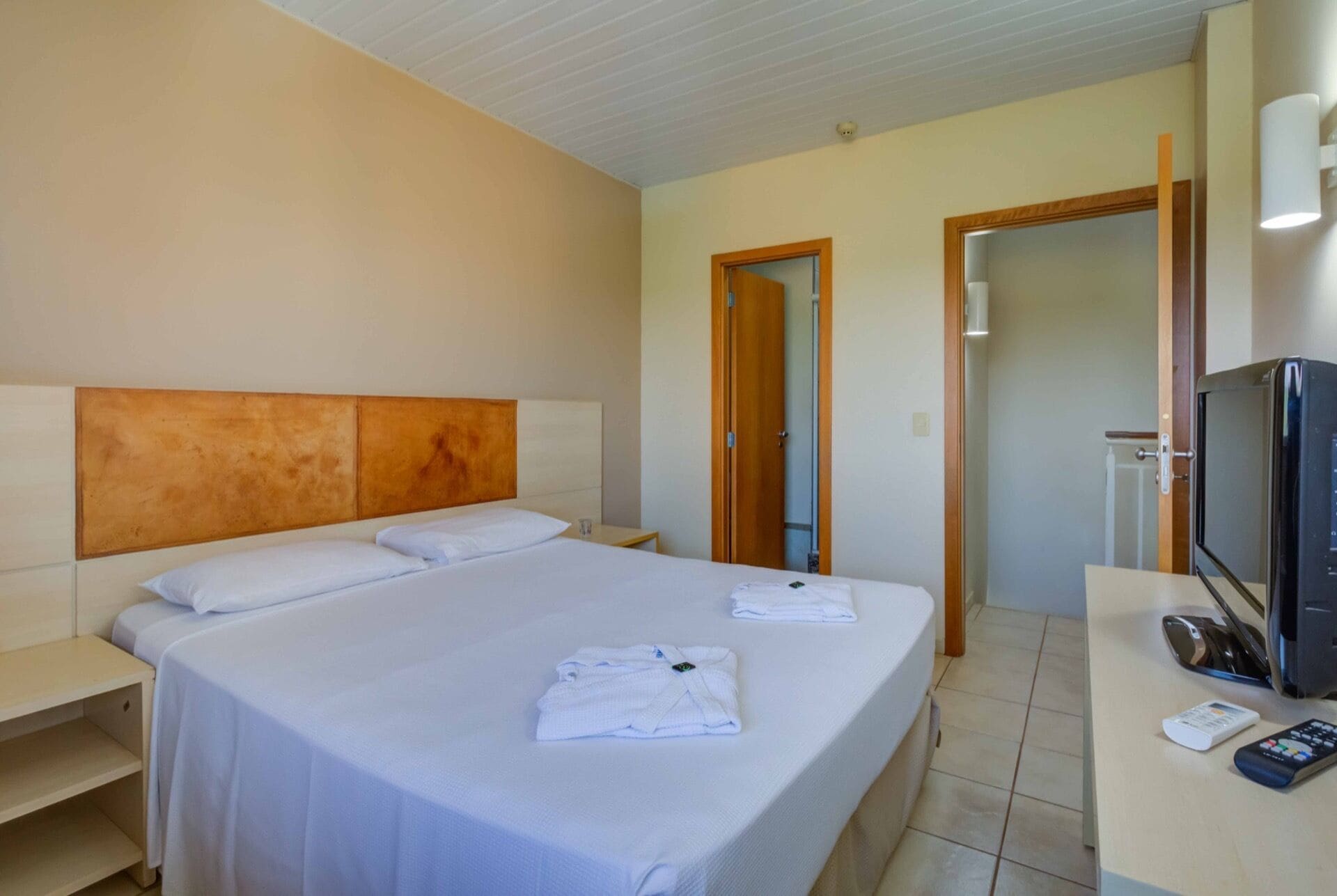 Ein Hotelzimmer mit einem großen Bett, einem Fernseher, einem Schreibtisch und einer Badezimmertür.
