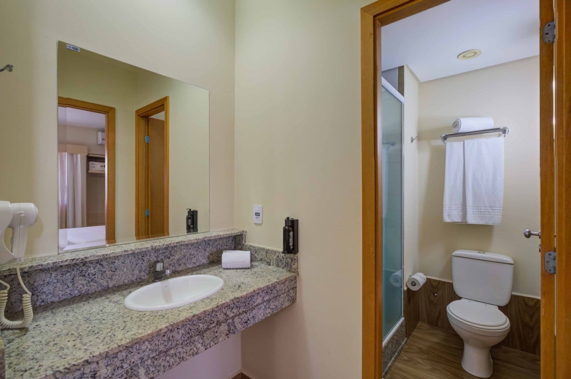 Un baño con encimera de granito, un lavamanos blanco, un espejo, un inodoro y una zona de ducha.