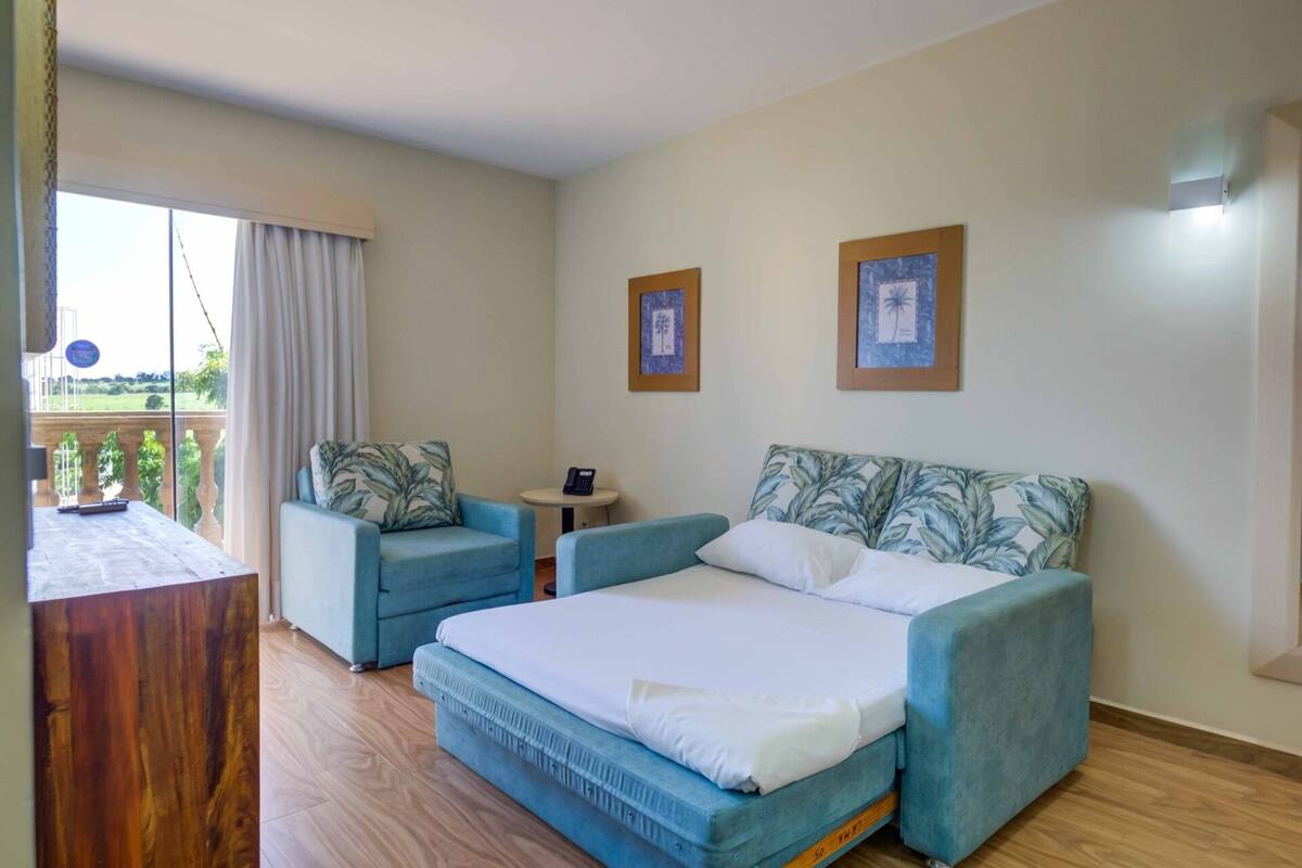 A bedroom with a bed, two armchairs, a small table, and a view of a balcony.