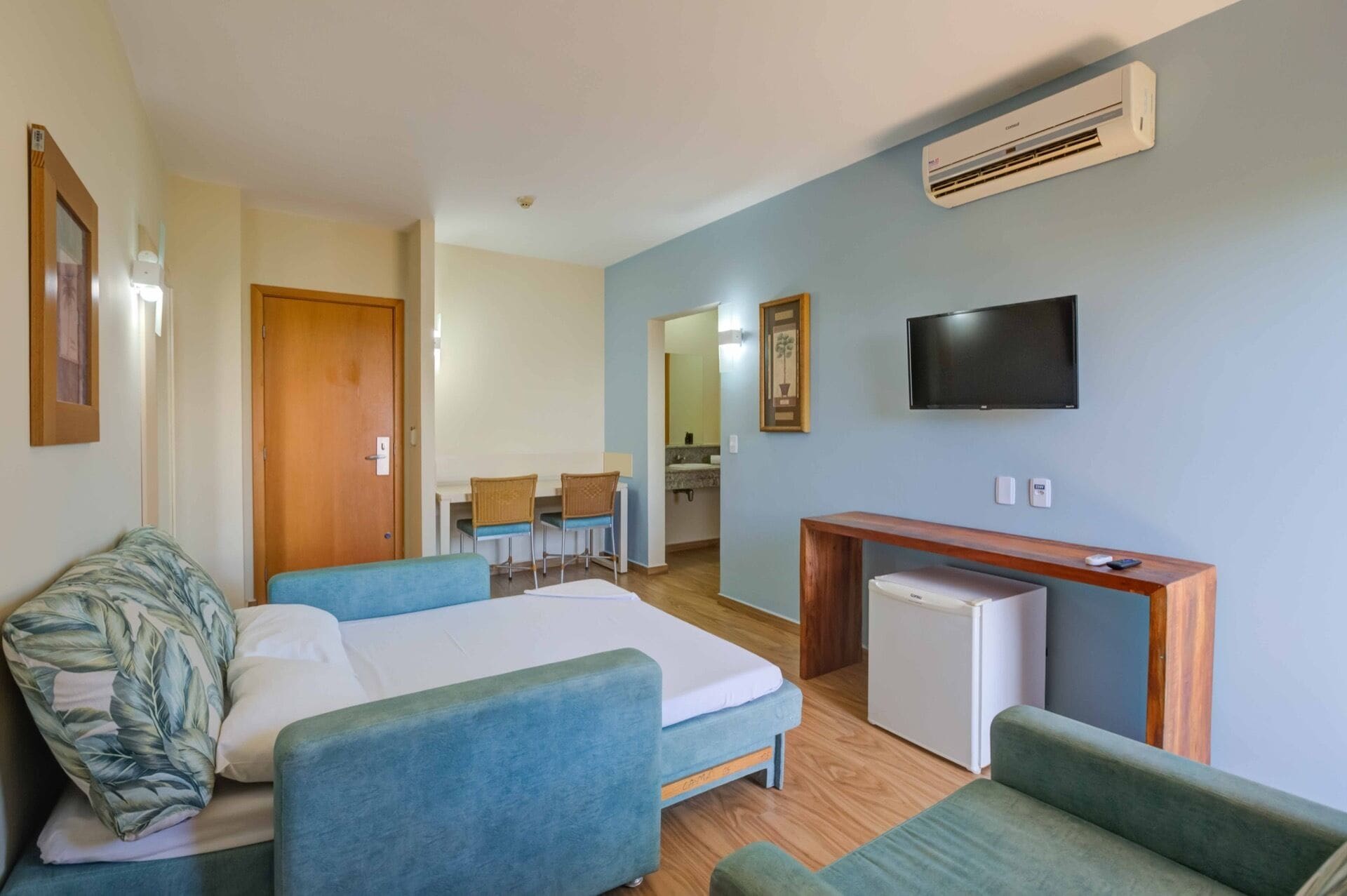 Een hotelkamer met een bed, twee banken, een bureau, een televisie en een airconditioning.