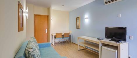 A compact living space with a sofa, a TV, a small fridge, and a dining area with chairs and a table.