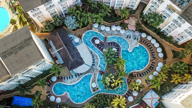 An aerial view of a resort with multiple swimming pools, palm trees, and a beach area.