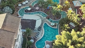 A hotel with a central swimming pool surrounded by lounge areas and palm trees.