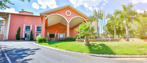 A building with a red facade, a covered entrance, and a well-maintained lawn.