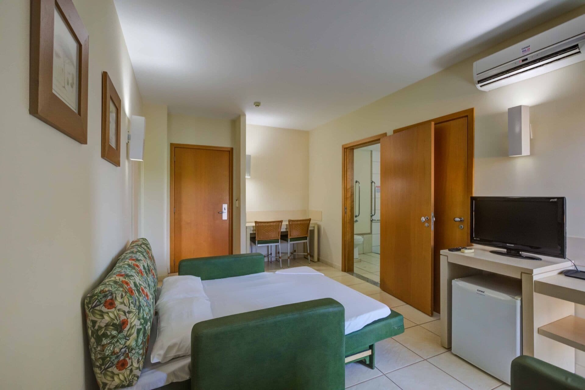 Een hotelkamer met twee bedden, een bureau met een televisie en een kleine koelkast.