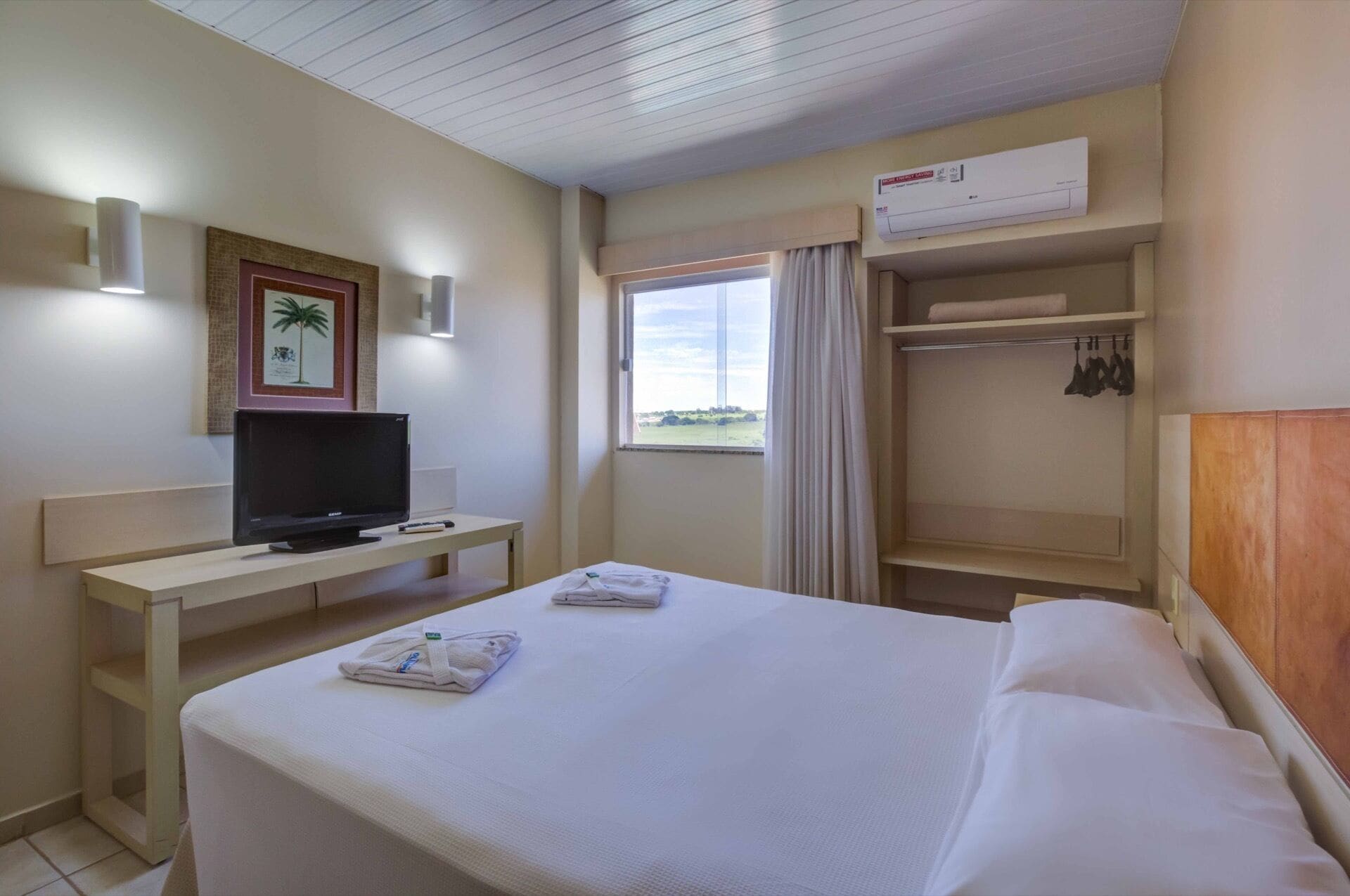 Habitació d'hotel amb un llit, un escriptori amb televisió, una finestra amb cortines i un armari.
