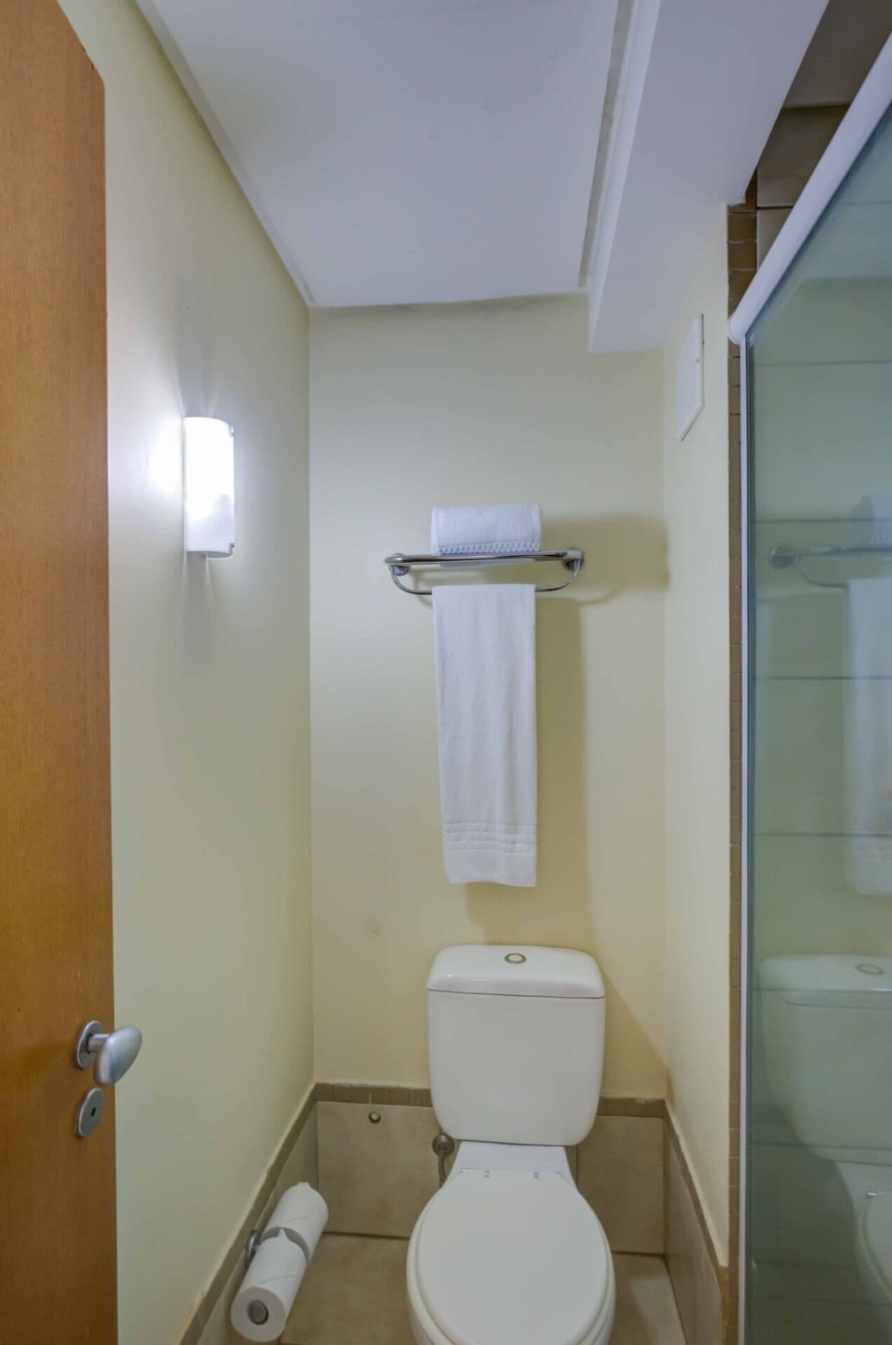 A small, compact bathroom with a toilet, a towel rack, and a toilet paper roll.