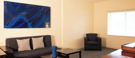 A modern room with a sofa, armchair, coffee table, and a large abstract painting on the wall.