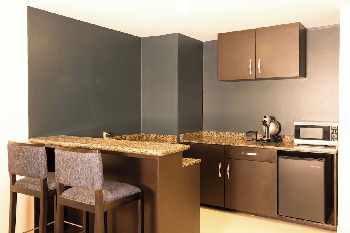 A compact kitchen with dark cabinetry, a granite countertop, a microwave, and two bar stools.