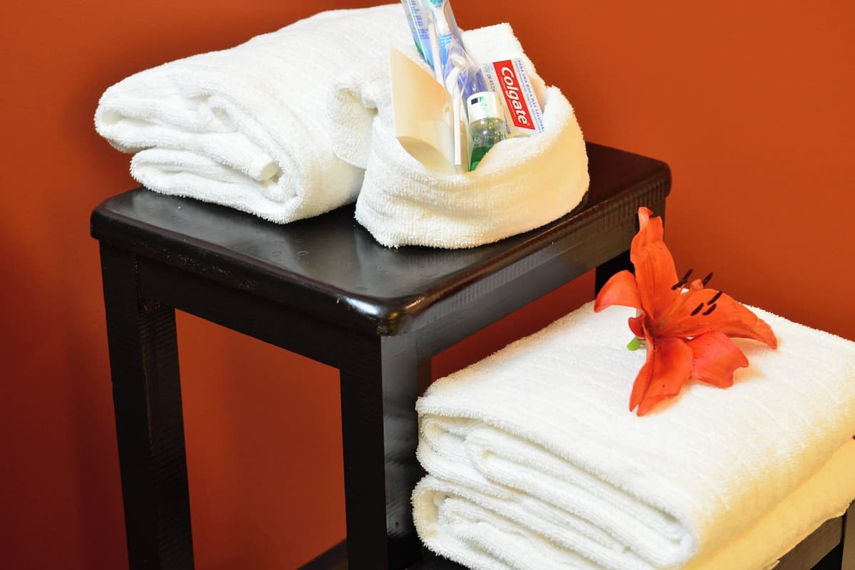 A stack of white towels on a black table with a red flower on top.