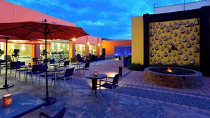 Un patio al aire libre con mesas y sillas, un hogar para fogata y una pared decorativa con diseños de gotas de agua.