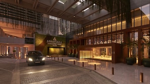 Un hall d'hôtel moderne, avec une voiture garée devant, une grande enseigne lumineuse et un espace spacieux agrémenté de plantes en pot.