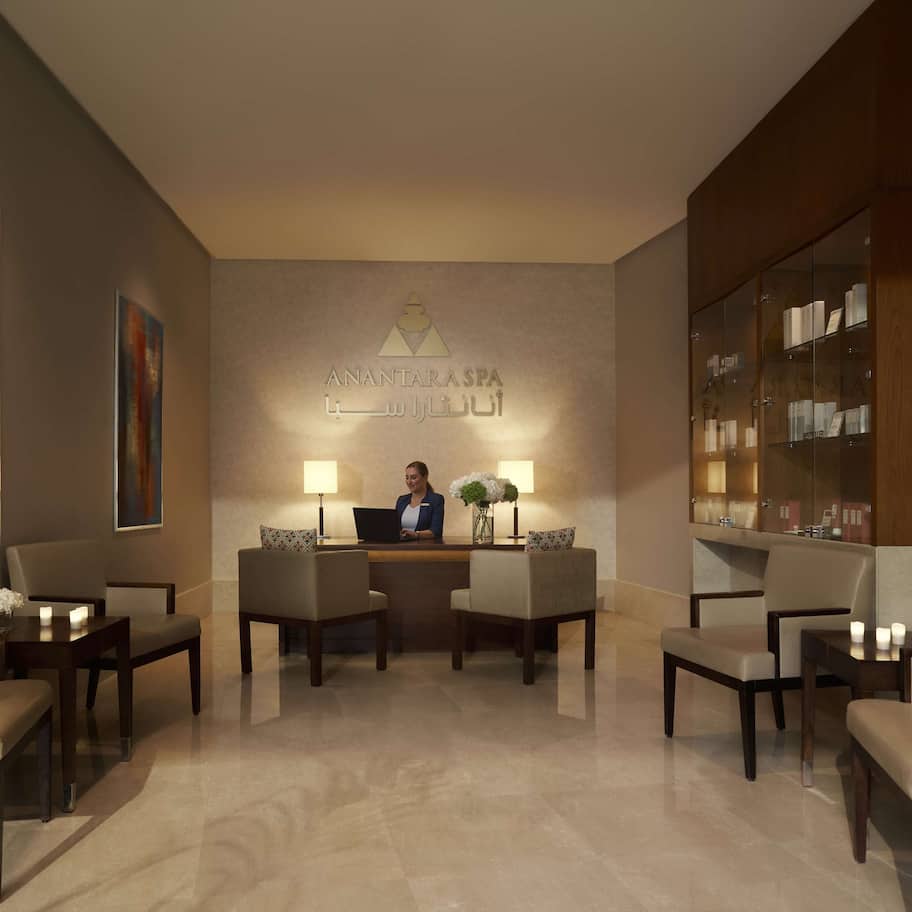 A reception area with a receptionist desk, two chairs, a small table with a vase of flowers, and a bookshelf.