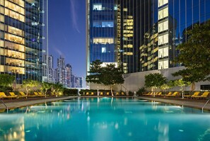 A swimming pool with lounge chairs and a city skyline in the background.