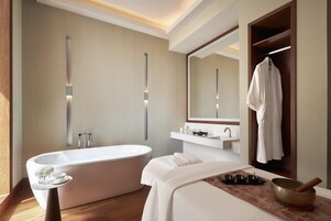 A modern bathroom with a freestanding bathtub, a vanity with a mirror, and a robe hanging on a wooden door.