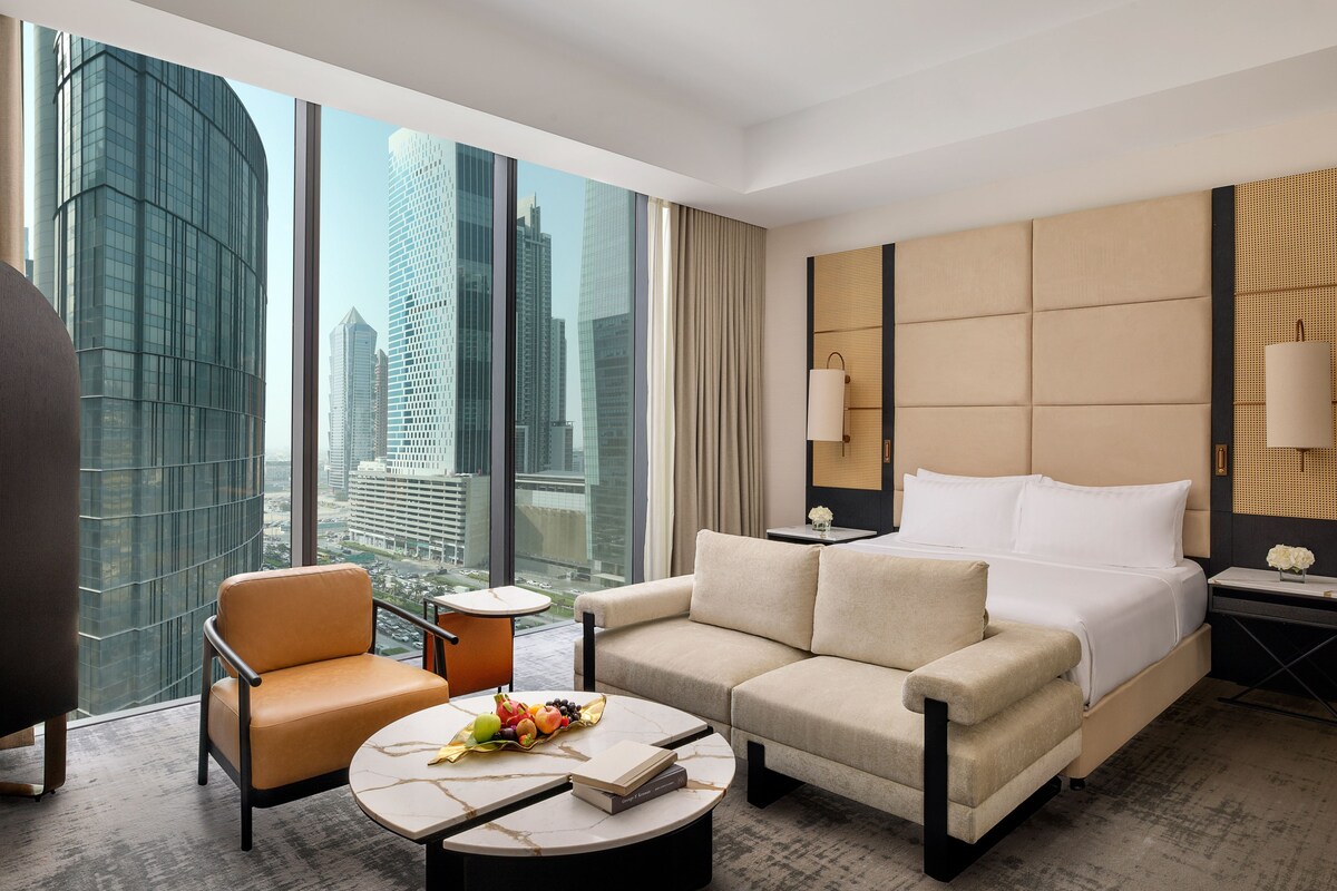 Ein modernes Hotelzimmer mit einem großen Bett, einer Couch, einem Couchtisch und Blick auf Wolkenkratzer der Stadt.