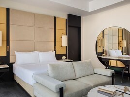 A modern hotel room with a large bed, a sofa, a desk, and a round mirror.