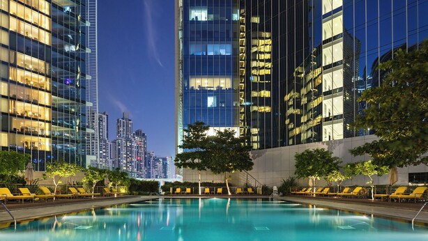 Un espace piscine moderne, situé dans un hôtel, offrant une vue sur les gratte-ciel au crépuscule.