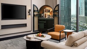 Une chambre d’hôtel moderne dotée d’une grande télévision, d’un coin bar, d’un canapé et offrant une vue sur la ville.