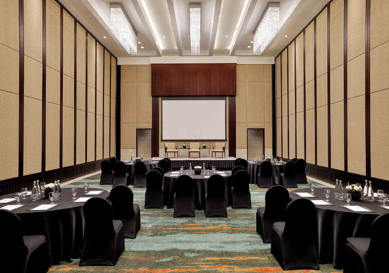 A conference room with a stage, multiple tables with chairs, and a carpeted floor.