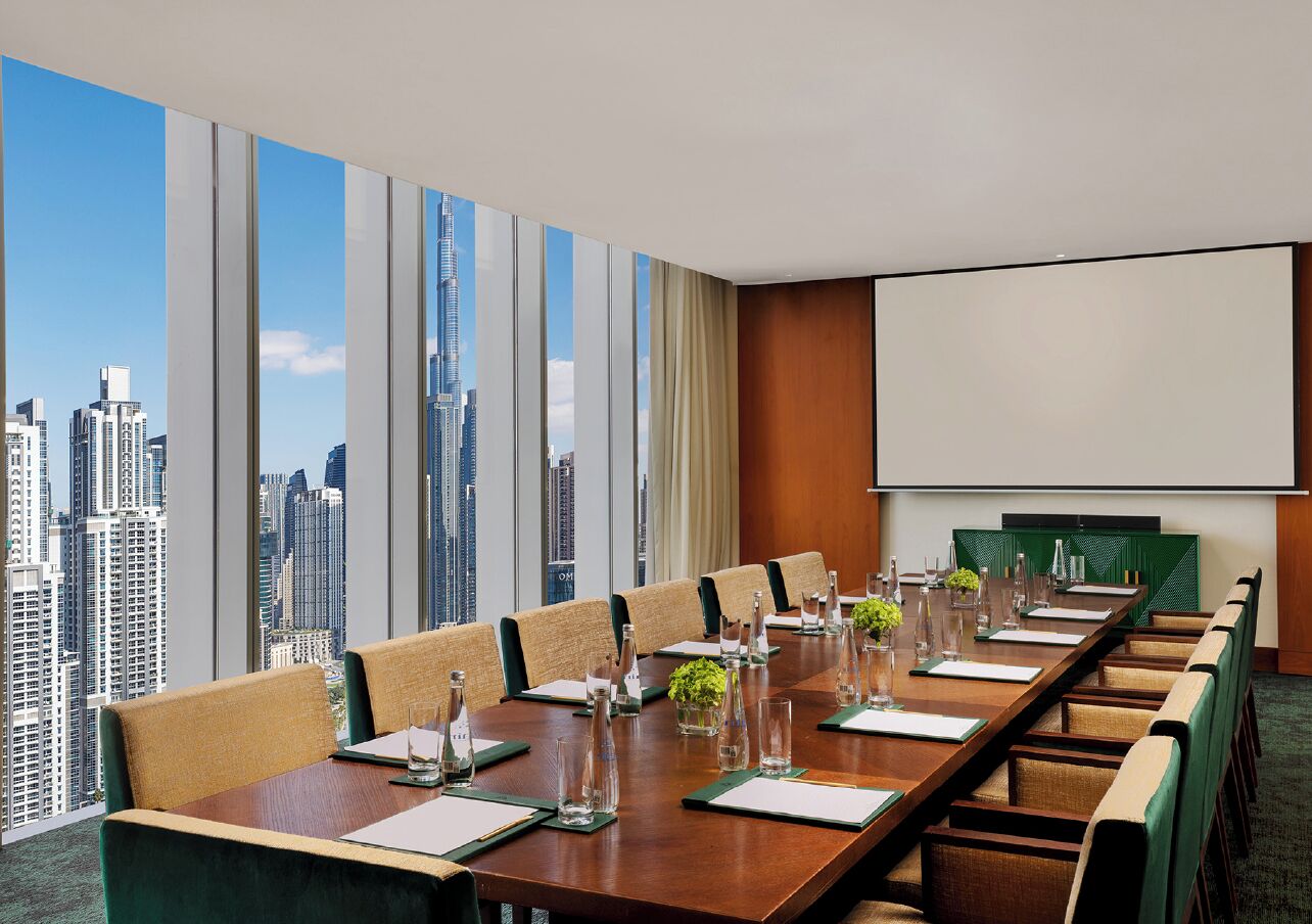 A conference room with a city view, a large table, and a screen.