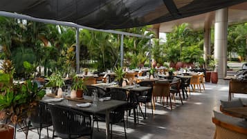 Un restaurante al aire libre con mesas y sillas, rodeado de plantas en macetas y árboles.