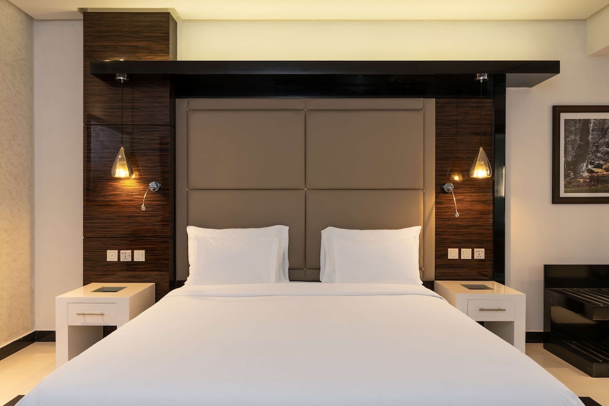 Una habitación de hotel moderna con una cama grande, dos mesitas de noche e iluminación colgante.