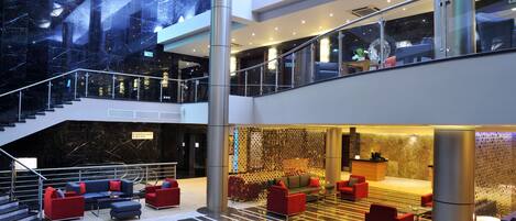 A modern hotel lobby with a spacious seating area, a staircase, and a reception desk.