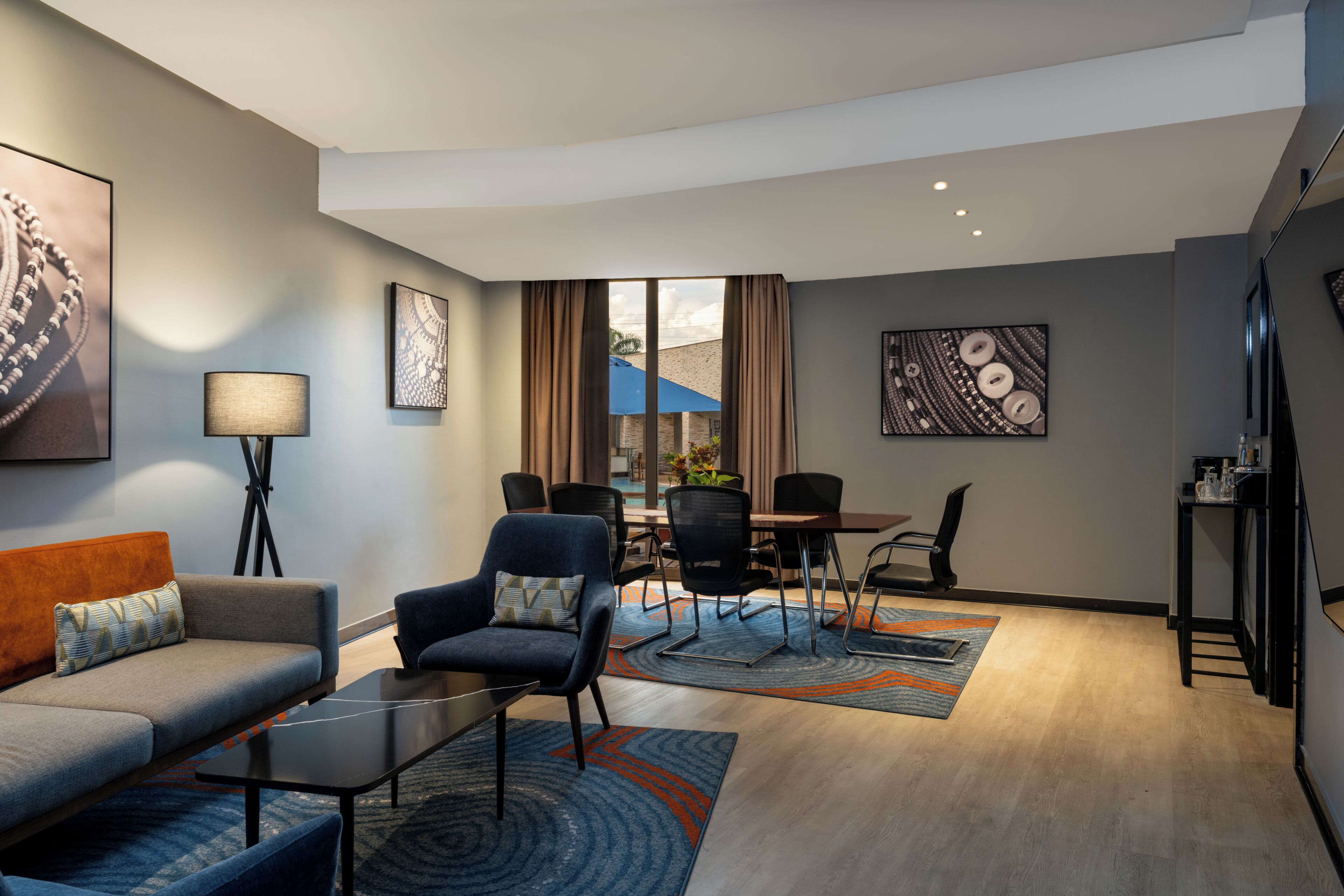 A modern hotel room with a sofa, armchair, dining table, chairs, and artwork on the walls.