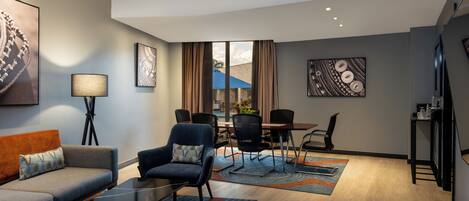 Una habitación de hotel moderna con sofá, sillón, mesa de comedor, sillas y obras de arte en las paredes.
