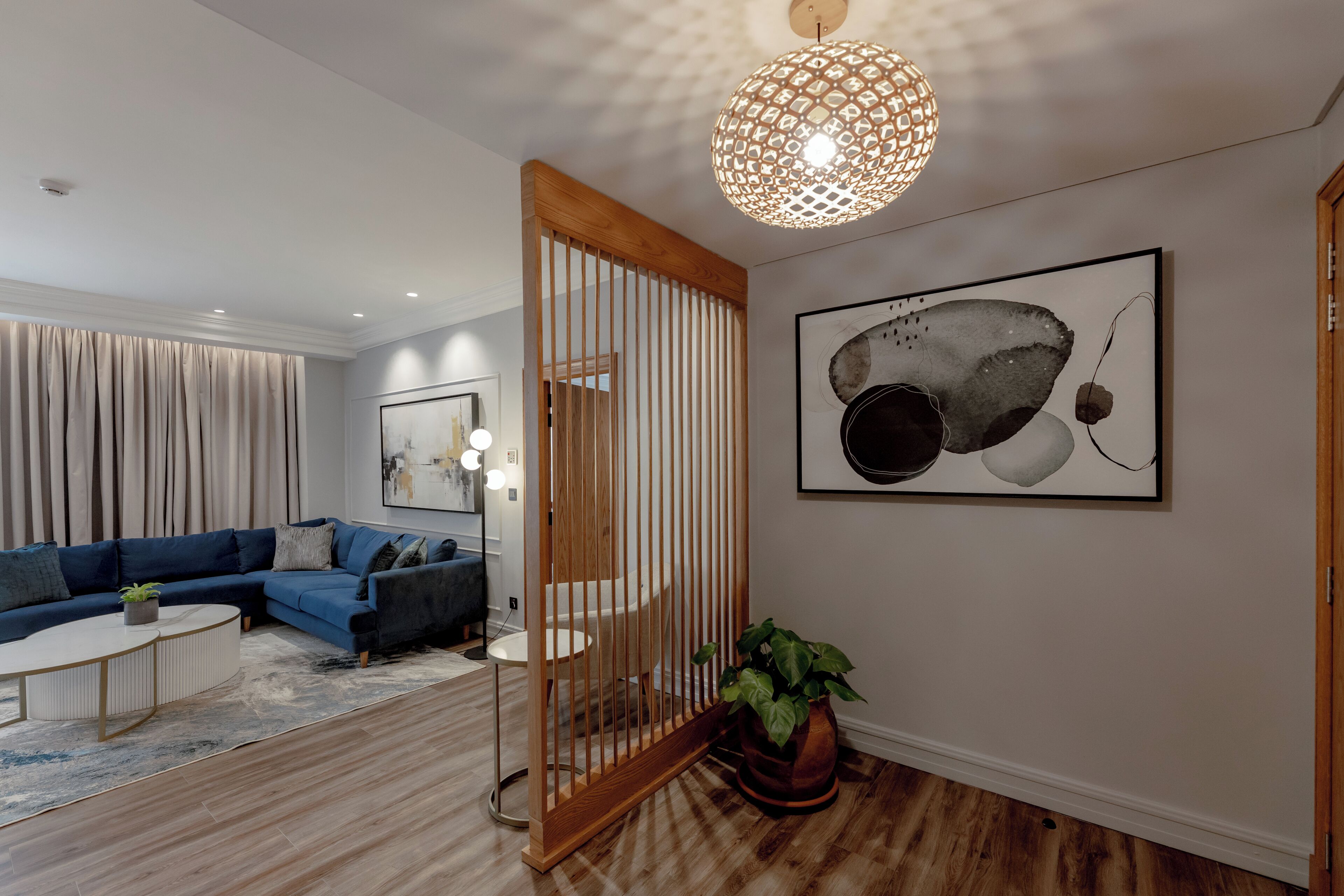 A modern living room with a sectional sofa, a round coffee table, a wooden partition, a potted plant, and a large abstract painting on the wall.