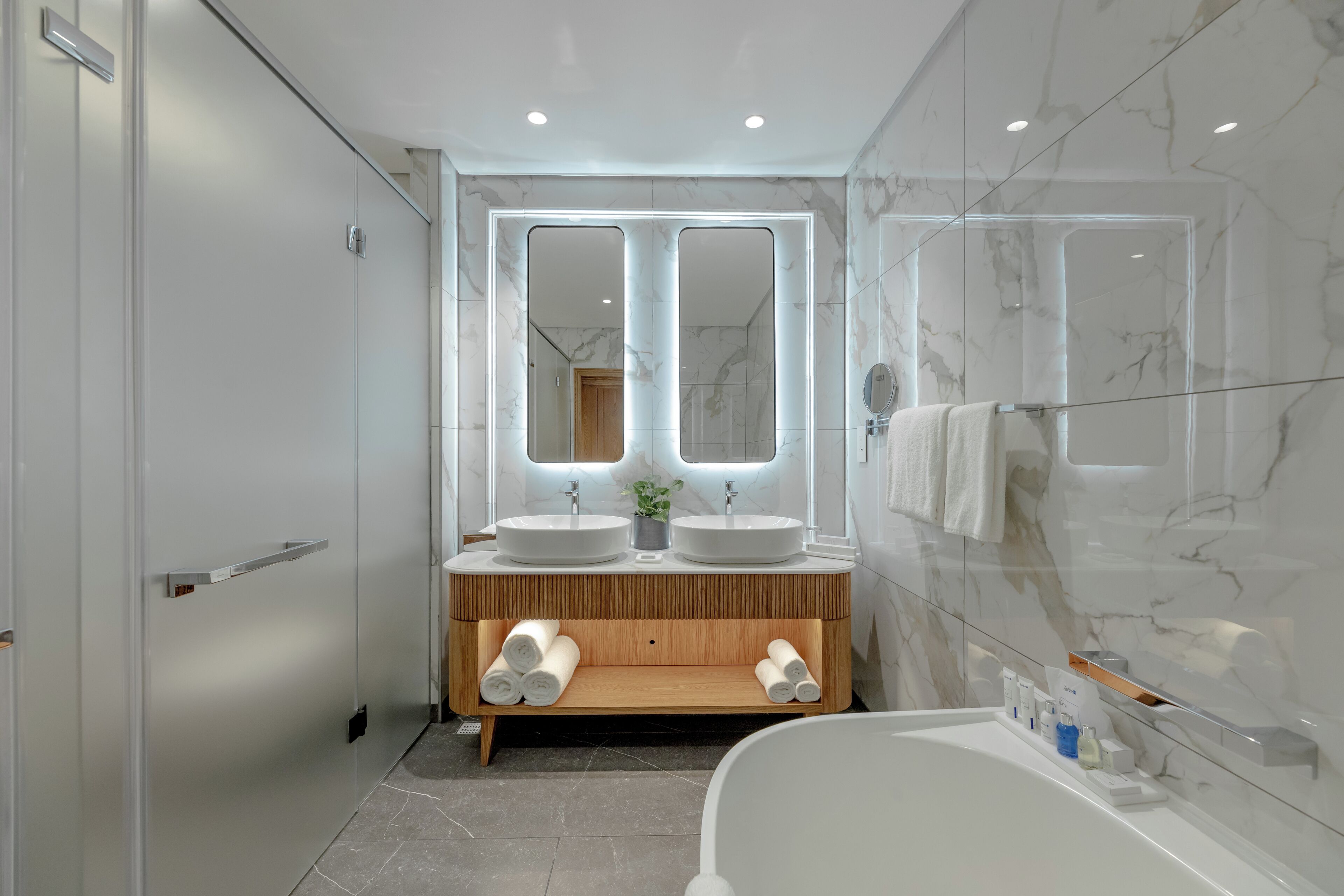 Un baño moderno con dos lavamanos, un mueble de tocador de madera, una cabina de ducha de vidrio y una bañera.