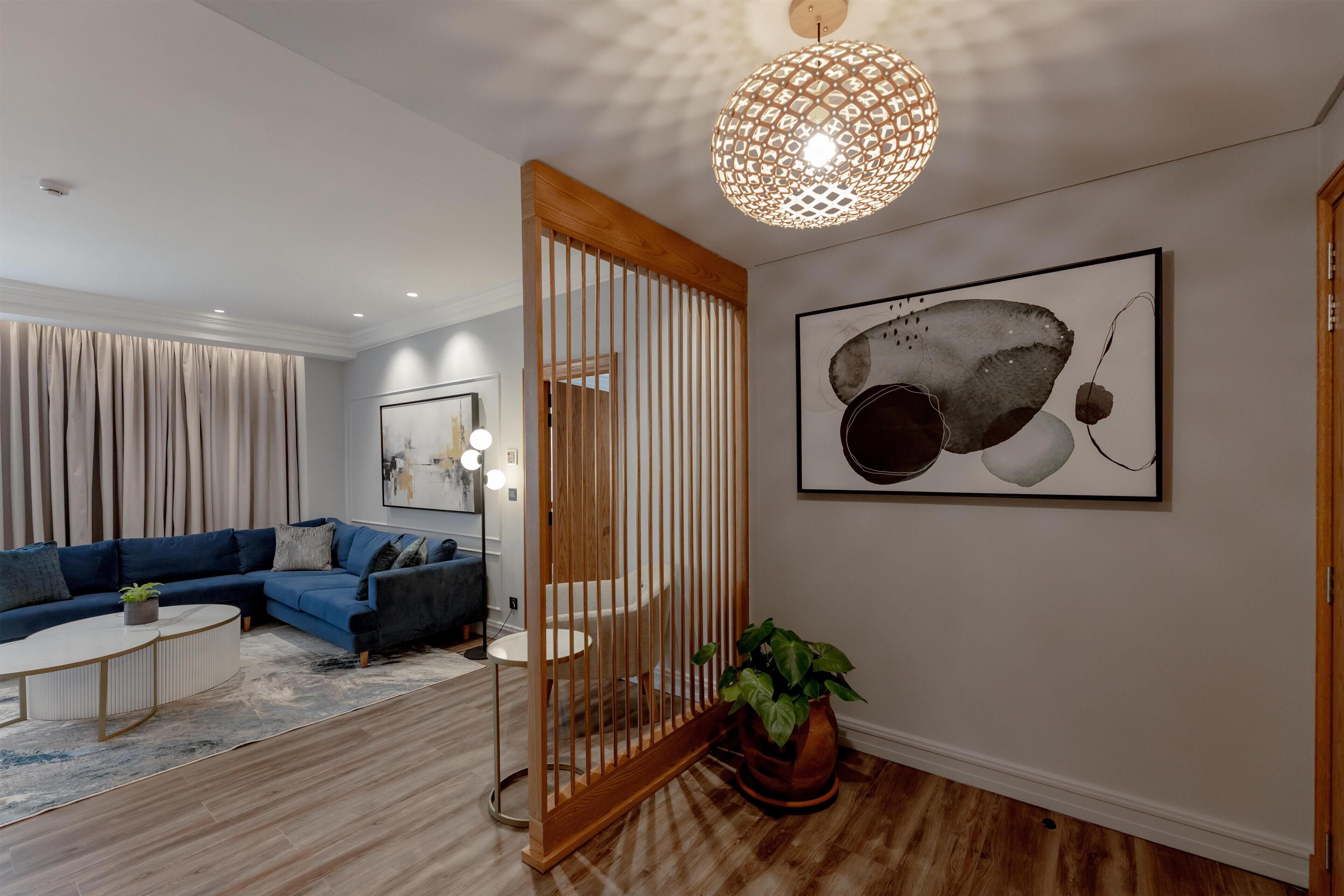 A modern living room with a sectional sofa, a round coffee table, a wooden partition, a potted plant, and a large abstract painting on the wall.