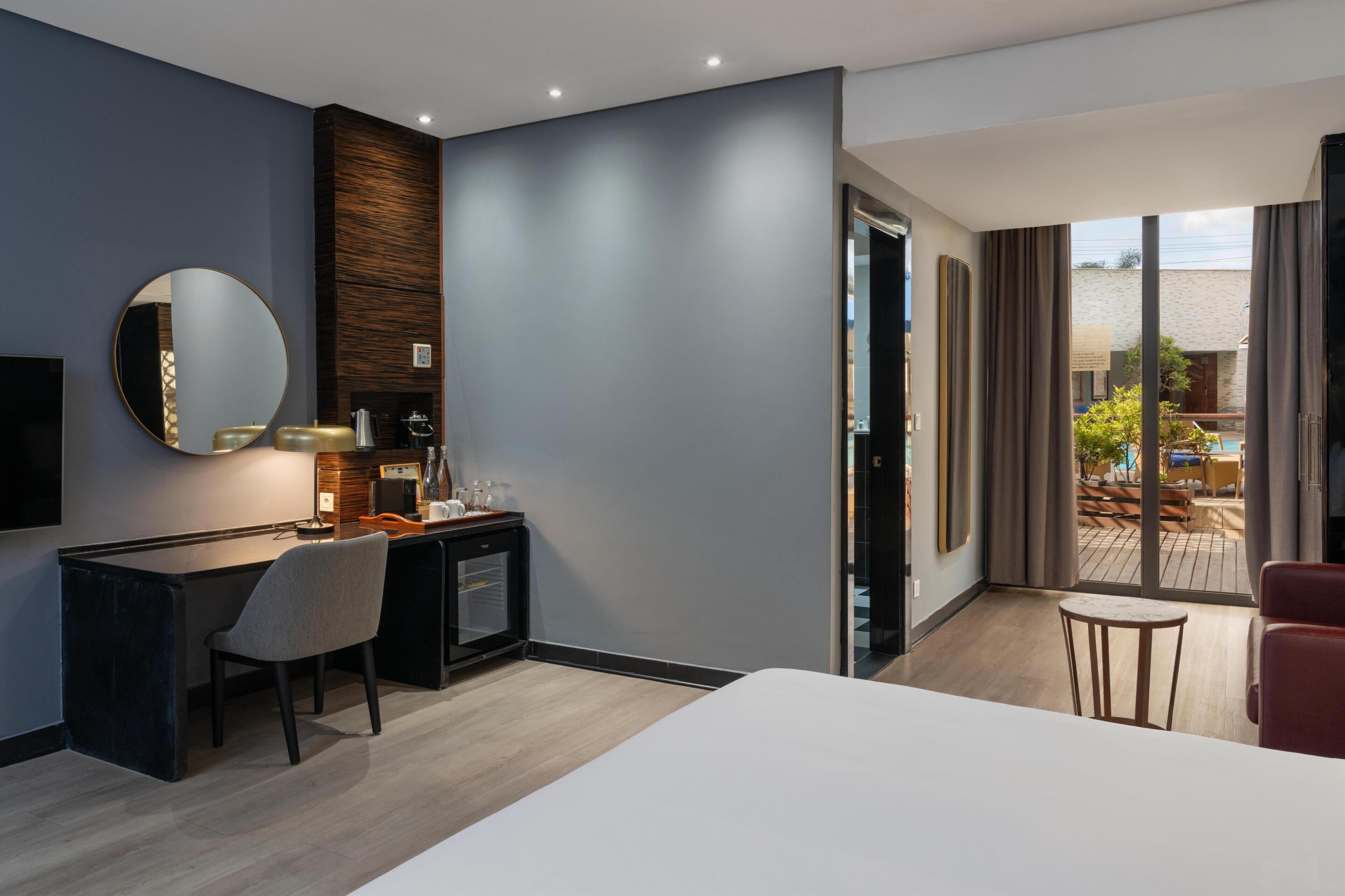 Camera d'albergo moderna con un letto grande, una scrivania con una sedia, uno specchio rotondo e vista sul patio esterno.