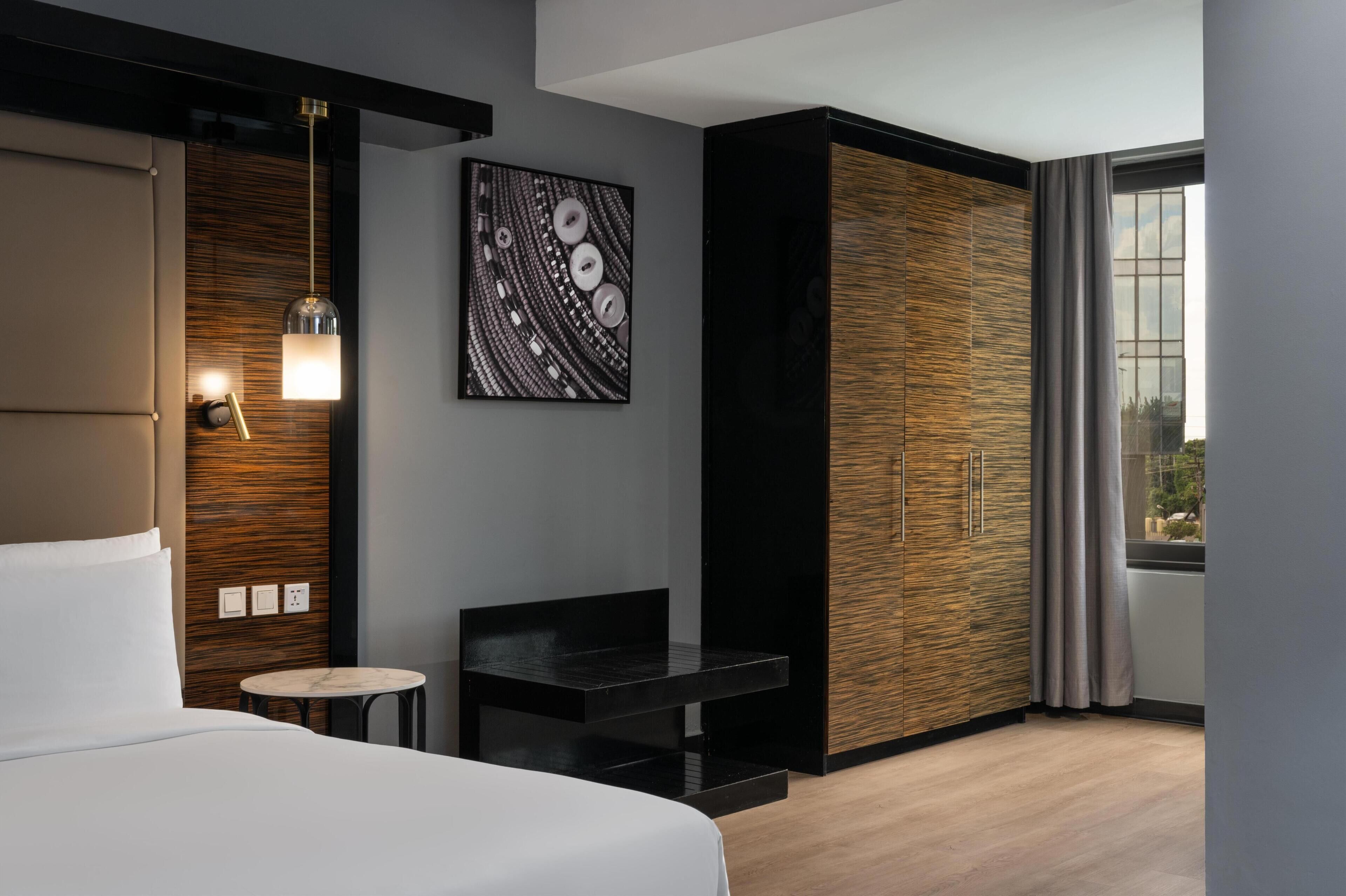 Ein modernes Hotelzimmer mit Bett, einem kleinen Tisch, einem Wandbild und einem Kleiderschrank.