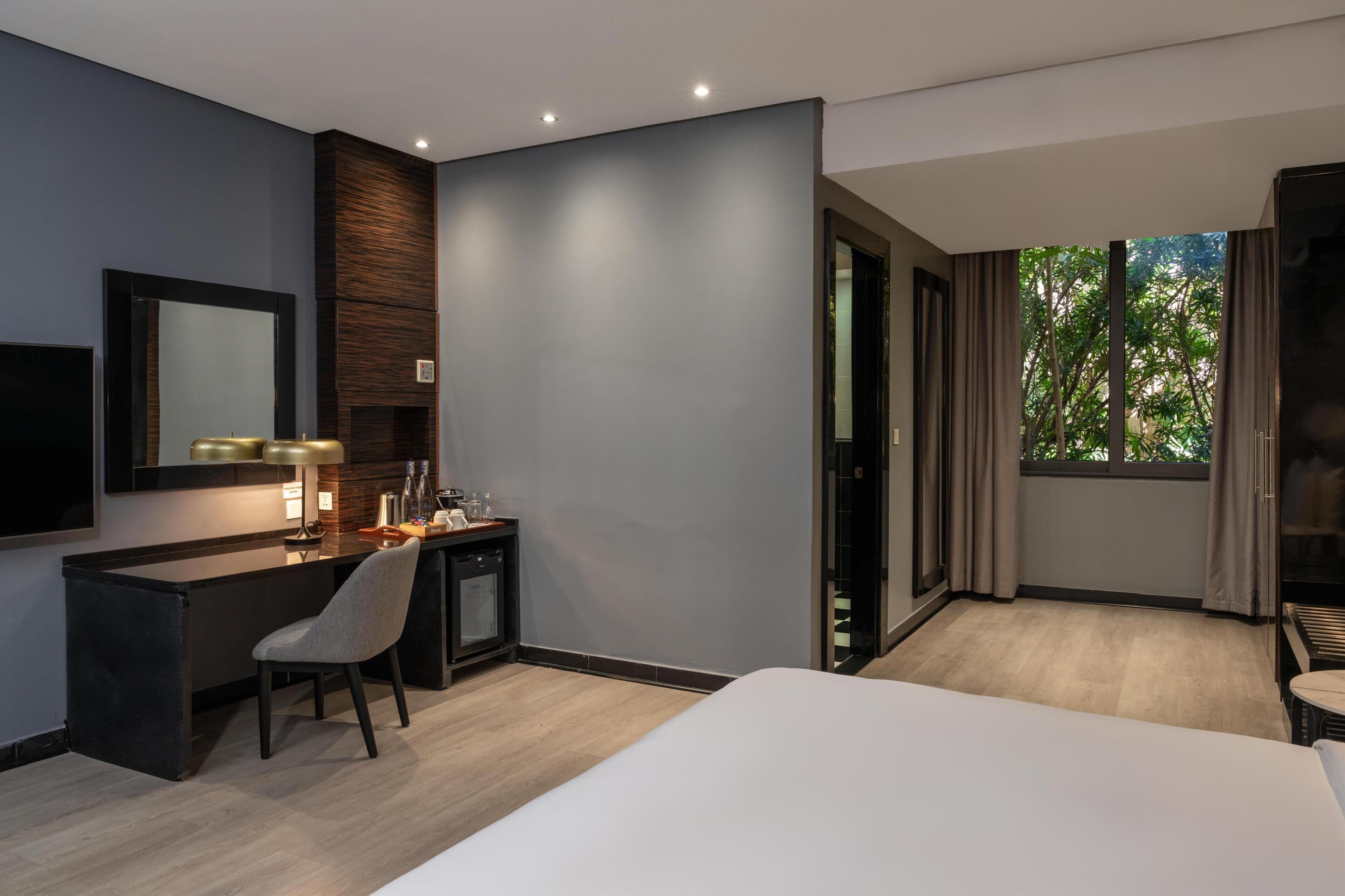 A hotel room with a bed, desk, chair, and a large window with curtains.