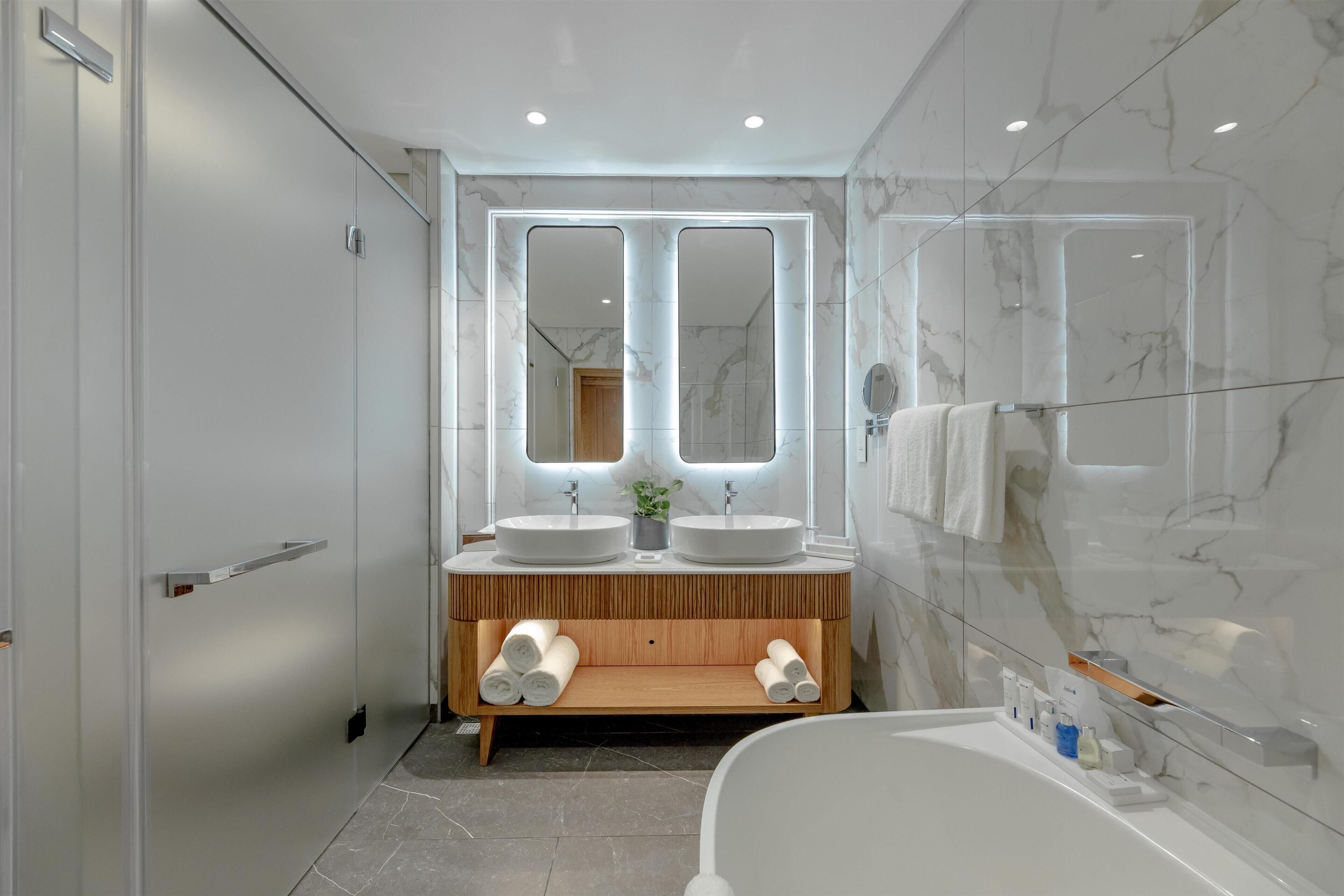 A modern bathroom with two sinks, a large mirror, and a glass-enclosed shower.