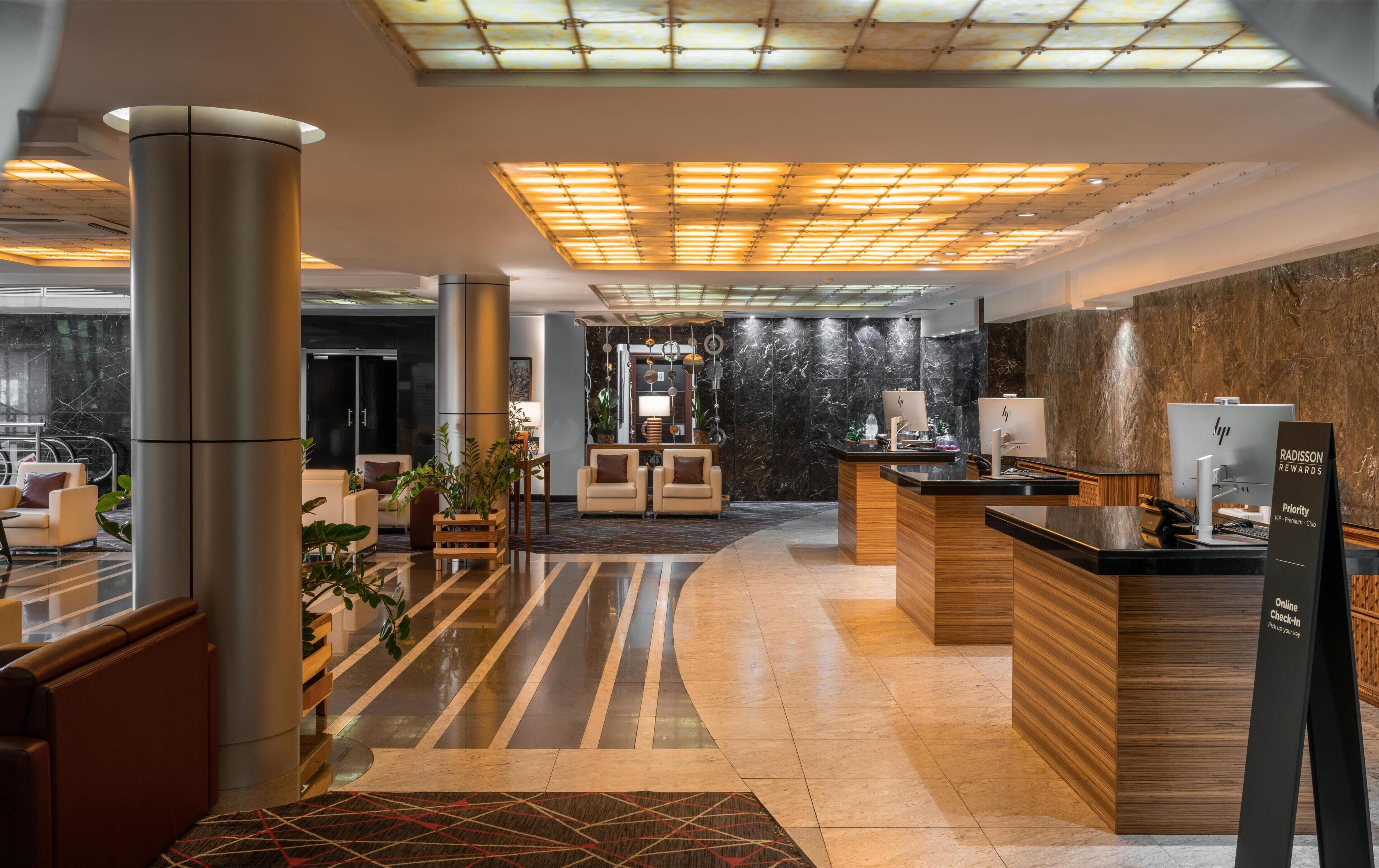 A modern hotel lobby with a reception desk, seating area, and a large column.